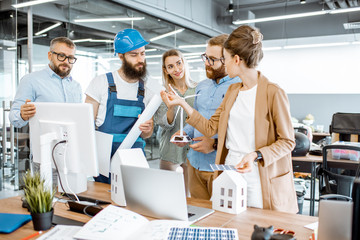 Wall Mural - Group of engineers and workman working on a project of alternative energy at the office with computer, wind turbine and solar panels model