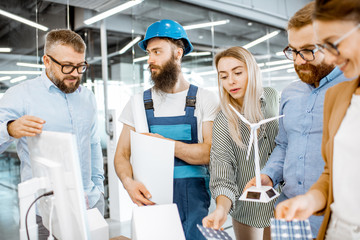 Sticker - Group of engineers and workman working on a project of alternative energy at the office with computer, wind turbine and solar panels model