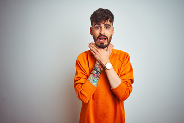 Poster - Young man with tattoo wearing orange sweater standing over isolated white background shouting and suffocate because painful strangle. Health problem. Asphyxiate and suicide concept.