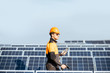 © rh2010 - Well-equipped worker in protective orange clothing servicing solar panels on a photovoltaic rooftop plant. Concept of maintenance and installation of solar stations