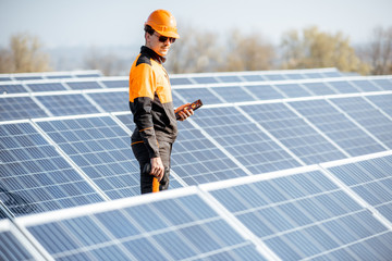 Wall Mural - portrait of a well-equipped worker in protective orange clothing examining solar panels on a photovo