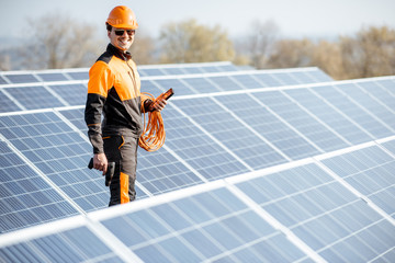 Wall Mural - Portrait of a well-equipped worker in protective orange clothing examining solar panels on a photovoltaic rooftop plant. Concept of maintenance and installation of solar stations