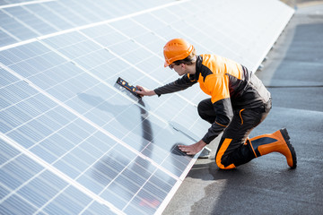Wall Mural - well-equipped worker in protective orange clothing installing solar panels, measuring the angle of i