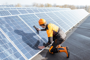 Wall Mural - well-equipped worker in protective orange clothing installing solar panels, measuring the angle of i