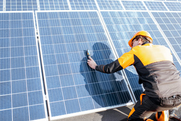 Wall Mural - well-equipped worker in protective orange clothing installing solar panels, measuring the angle of i