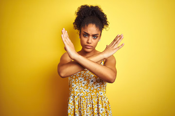 Sticker - African american woman wearing casual floral dress standing over isolated yellow background Rejection expression crossing arms doing negative sign, angry face