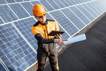 Wall Mural - Portrait of an engineer in protective workwear carrying out service of solar panels with digital tablet and blueprintson a photovoltaic rooftop plant