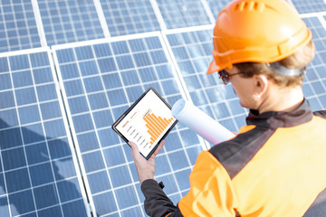 Wall Mural - workman examining genaration of solar power plant, holding digital tablet with a chart of electricit