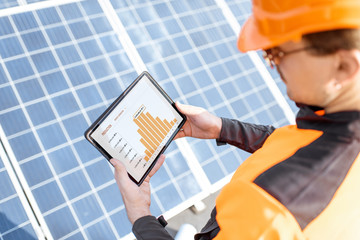 Wall Mural - workman examining genaration of solar power plant, holding digital tablet with a chart of electricit