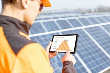 Wall Mural - workman examining genaration of solar power plant, holding digital tablet with a chart of electricit