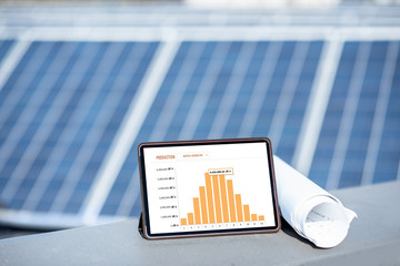 Composition of blueprints and digital tablet with a chart of electricity production on a solar power plant outdoors. Electricity production monitoring concept