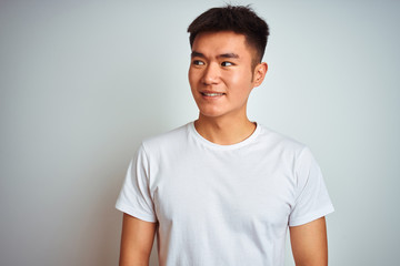 Young asian chinese man wearing t-shirt standing over isolated white background smiling looking to the side and staring away thinking.