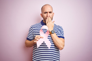 Sticker - Young man holding pink brest cancer ribbon over isolated background cover mouth with hand shocked with shame for mistake, expression of fear, scared in silence, secret concept