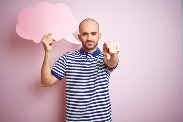 Wall Mural - Young man holding speech bubble with blank space for message over pink isolated background pointing with finger to the camera and to you, hand sign, positive and confident gesture from the front