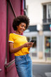 © mimagephotos - happy young african american woman looking at cellphone outside in city