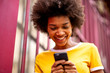 © mimagephotos - Close up of smiling young african american woman looking at mobile phone outside