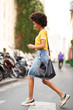 © mimagephotos - Full body side of young african american woman walking with cellphone on street