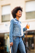 © mimagephotos - happy young african american woman walking in city with shopping bag and drink
