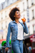 © mimagephotos - happy young black woman walking in city with shopping bag and drink