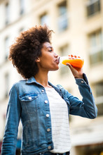 Happy Young Black Woman Drinking From Juice Bottle In City