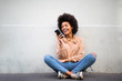 © mimagephotos - happy young african american woman sitting on floor with cellphone