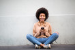 © mimagephotos - happy young african american woman sitting on floor with mobile phone