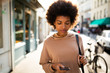 © mimagephotos - young black woman walking with mobile phone in city