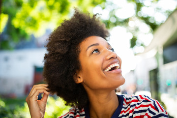 Wall Mural - Close up happy young black woman smiling with afro hair in park and looking up