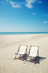 Wall Mural - pair of empty deck chairs sitting together on a deserted beach with calm blue sea on the horizon