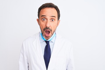 Poster - Middle age scientist man wearing coat and medical mask over isolated white background afraid and shocked with surprise expression, fear and excited face.