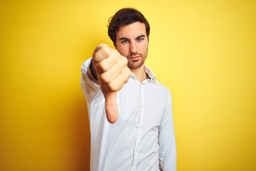 Wall Mural - Young handsome businessman wearing elegant shirt standing over isolated yellow background looking unhappy and angry showing rejection and negative with thumbs down gesture. Bad expression.