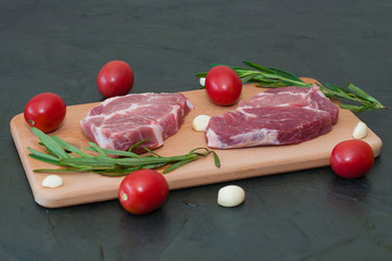 Wall Mural - Raw pork steaks with red tomatoes, rosemary and garlic on a cutting board.