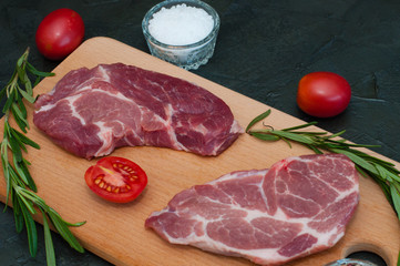 Wall Mural - Pork, raw steaks and spices, garlic, salt, pepper, sliced tomatoes and rosemary on cutting board, close-up