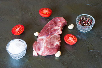 Wall Mural - Flat lay, cooking process of pork steak, salt, pepper, garlic and sliced tomato on gray concrete background