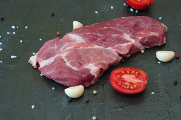 Wall Mural - cooking process pork steak, meat sprinkled with salt and pepper, garlic cloves and sliced tomato on gray concrete background, view from the top and from the side