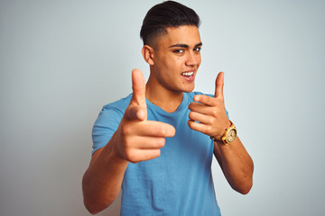 Young brazilian man wearing blue t-shirt standing over isolated white background pointing fingers to camera with happy and funny face. Good energy and vibes.