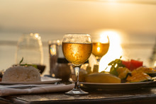 Two Wine Glasses On Wooden Table Near Sea On The Tropical Beach During Sunset