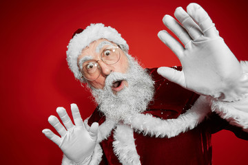 Wall Mural - Waist up portrait of surprised Santa Claus looking at camera while standing against red background in studio, copy space