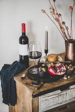 Wine And Snack Set. Glass And Bottle Of Red Wine, Board With Cheese, Fruit, Almonds And Olives, Decorative Cotton Flowers On Kitchen Counter, White Wall At Background. Winery Concept