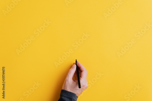 Fotografía Male hand writing on a blank yellow surface with black marker