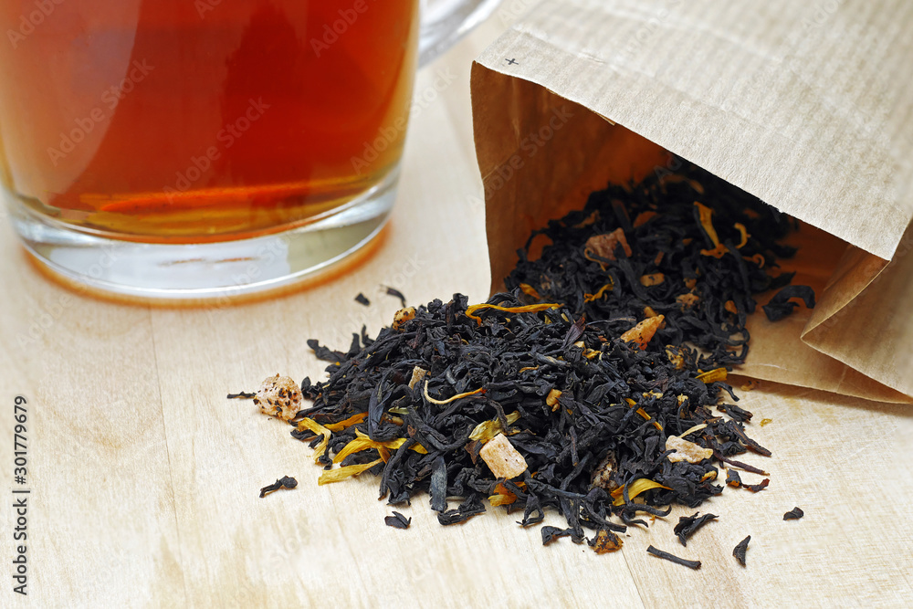 close-up of fruit and herbal black loose leaf tea in paper bag and cup of tea
