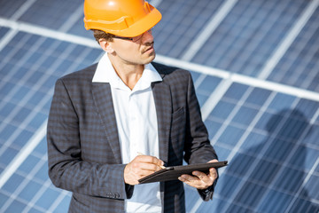 Wall Mural - Businessman dressed in the suit with protective helmet working with digital tablet on a solar station. Concept of successful investment in alternative energy