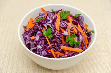 Red cabbage coleslaw with carrots and parsley in a white bowl on a linen surface. Healthy vegetarian and vegan food. Low calorie diet concept