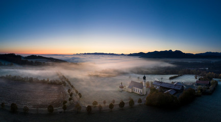 Wall Mural - beautiful foggy autumn morning in bavaria - aerial view of wilparting church before alps in chiemgau
