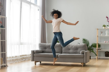 Happy African American woman jumping in living room, celebrating success