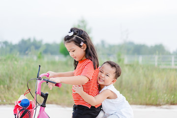 Wall Mural - Little sister and her baby brother ride bicycle together.Toddler kid playing with sibling.Cute girl and baby boy relax at the park in Japan.Family with children at home. Love, trust and tenderness.