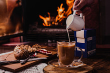 Pouring Milk From Porcelain Milk Jug Into Cup Filled With Tea - White Tablecloth And Fire Background. Winter Mood