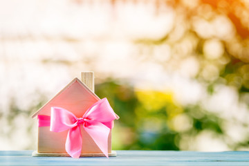 Home model tied with pink ribbon on bokeh in the public park, The buy new house or real estate as gift to family or the one loved concept.