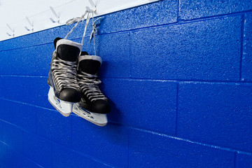 Wall Mural - Hockey skates hanging in locker room over blue background with copy space 