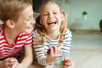 portrait of two cheerful children laying on the floor and playing with colorful dices